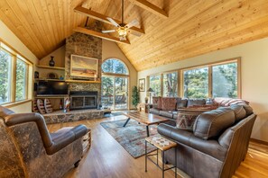 A spacious living room with a stone fireplace, leather sofas, and large windows offering a view of the outdoors. - Fox Haven at Summerwood Neighborhood, Community Pool+Clubhouse, Private Decks (Dillon)