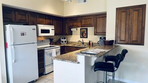 A kitchen with wooden cabinets, a white refrigerator, a microwave, a stove, and a coffee maker. There is a granite countertop and two bar stools. - Eastview Oasis by Mesquite Vacation Rentals near Wolf Creek Golf Course with $510 in free daily activities (Mesquite)