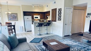 A modern living room with a sofa, coffee table, and patterned rug. A kitchen with wooden cabinets and a microwave is visible in the background. - Eastview Oasis by Mesquite Vacation Rentals near Wolf Creek Golf Course with $510 in free daily activities (Mesquite)