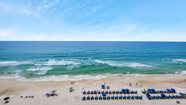 Une plage bordée de rangées de transats et de parasols, un rivage sablonneux et l’océan.
