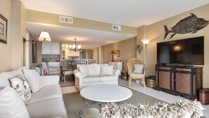A spacious living room with a white sofa, a round coffee table, and a television on a cabinet.