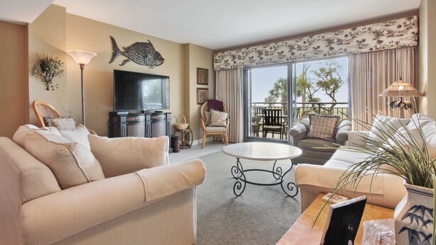 A living room with a sofa, a coffee table, a TV, and a balcony with outdoor furniture.
