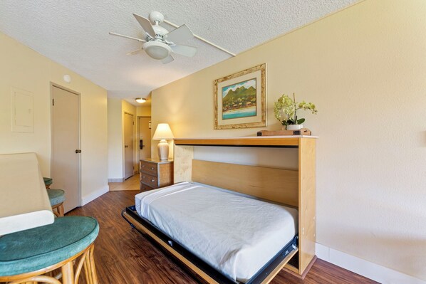 Une chambre d’hôtel de taille réduite, avec un lit superposé, une chaise, une table de chevet avec une lampe et un tableau encadré au mur.