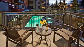 Un balcone con due sedie, un tavolo e vista su una piscina e degli edifici.