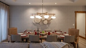 Zona pranzo con un tavolo rotondo apparecchiato per sei persone, circondato da sedie, un lampadario e un elemento decorativo a parete.