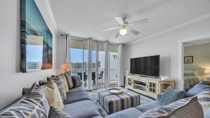Uma sala de estar moderna com um sofá cinzento, um banquinho e uma televisão de tela plana.
