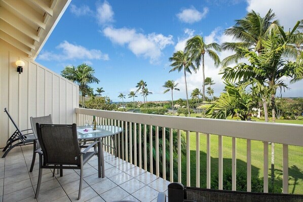 A balcony with a table and chairs, overlooking a lawn with palm trees and a clear sky.