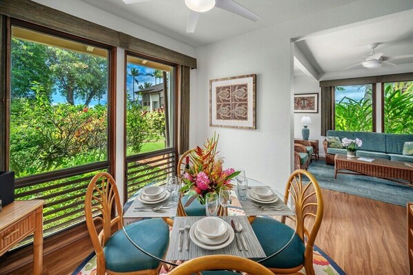 Un coin repas avec une table dressée pour quatre personnes, de grandes fenêtres donnant sur un paysage verdoyant et un espace détente avec un canapé et une table basse.