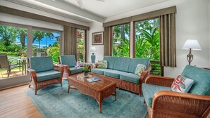 A spacious living room with wicker furniture, large windows, and a ceiling fan. - Kahala 713 Poipu Beach Ocean By Suite Paradise (Koloa)