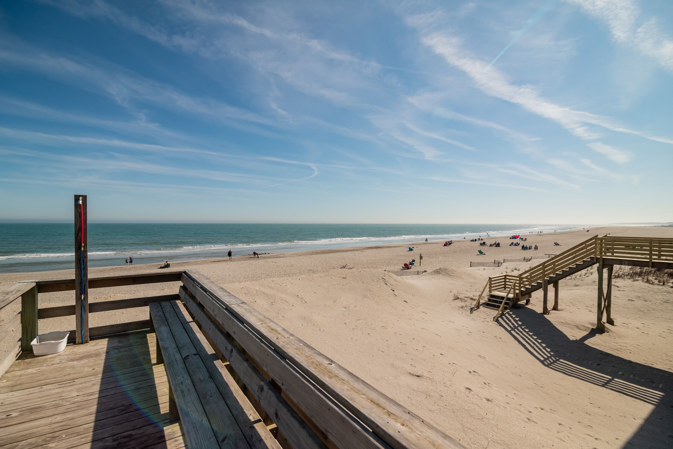 A wooden boardwalk leading to a sandy beach with a wooden staircase and a viewing platform.
