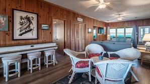 A wooden-paneled room with a bar area, wicker furniture, and a view of the ocean.