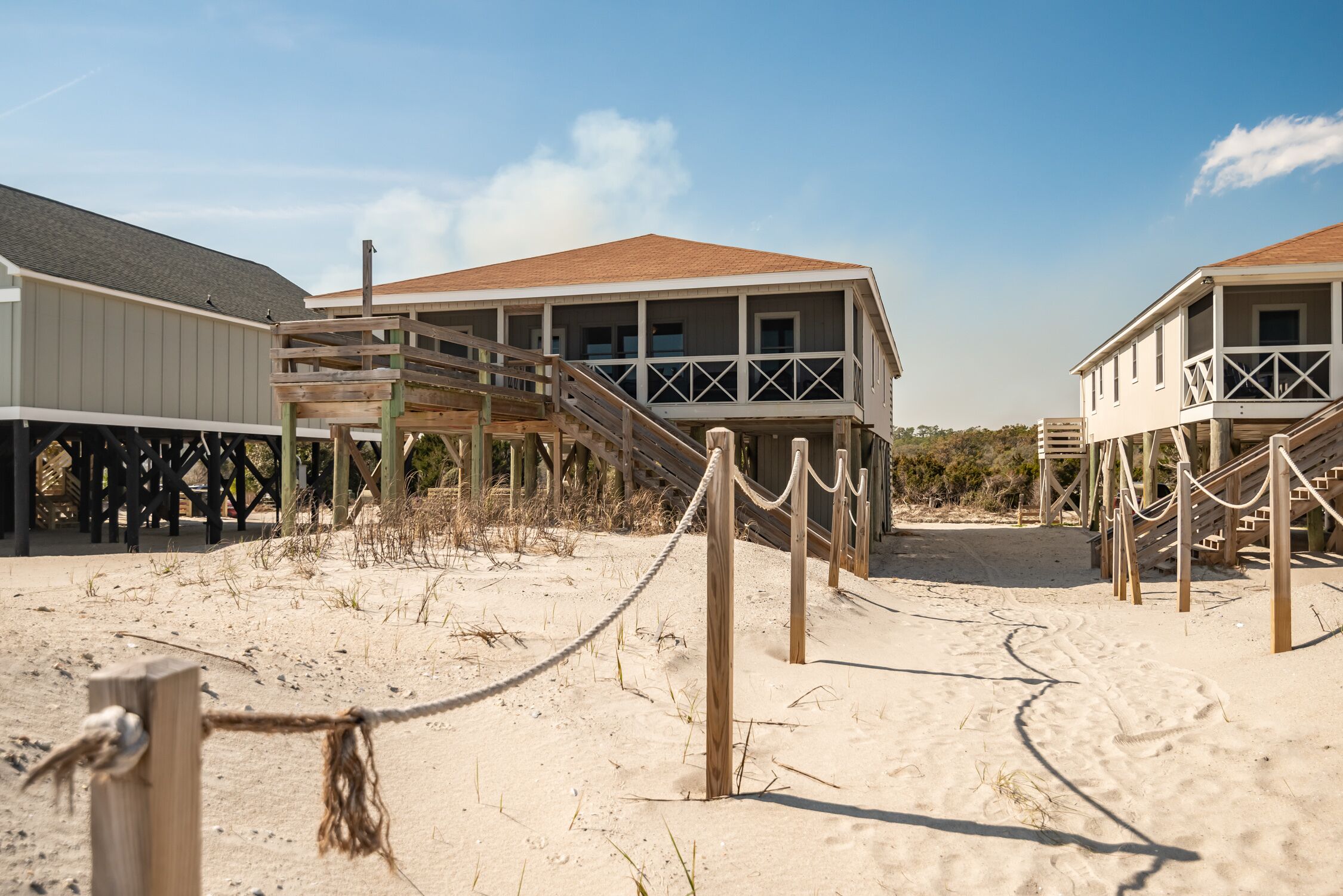 Una propiedad frente a la playa con pasarelas de madera que conducen a estructuras elevadas, una playa de arena y un cielo despejado.