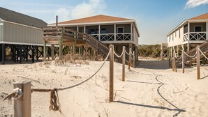 A beachfront property with wooden walkways leading to elevated structures, a sandy beach, and a clear sky.