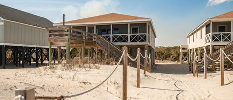 A beachfront property with wooden walkways leading to elevated structures, a sandy beach, and a clear sky.