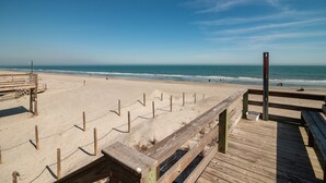A wooden boardwalk leading to a sandy beach with a clear view of the ocean.