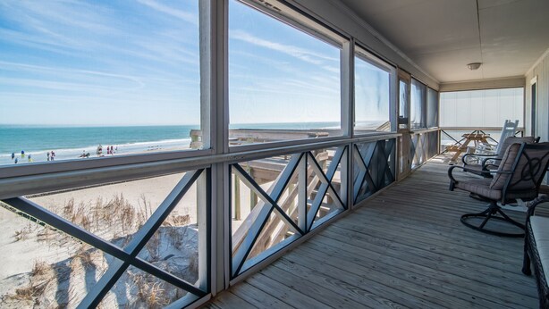 A wooden deck with a view of the beach and ocean.