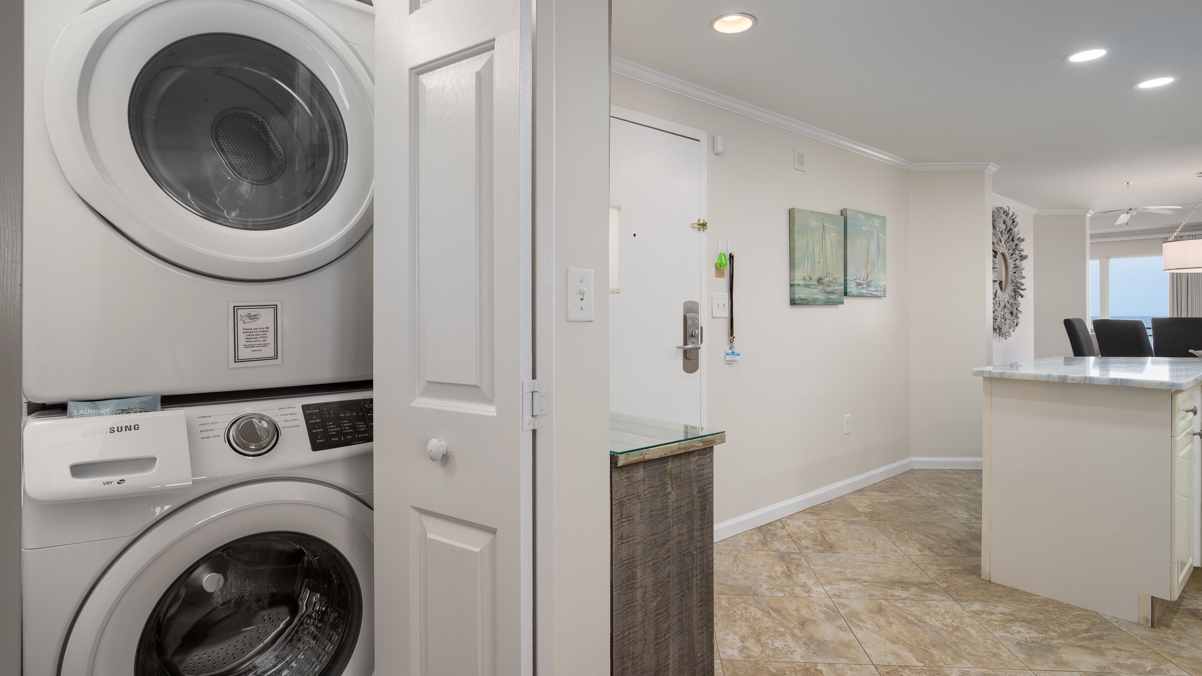 A laundry room with two front-loading washers, a countertop with a sink, and a dining area with chairs and a table.