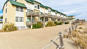 Un hilera de edificios de motel frente a la playa, con balcones y un paseo marítimo de arena.