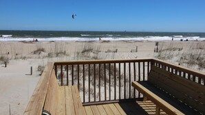 Una terraza de madera con vista a una playa y el océano, con una cometa volando en el cielo.