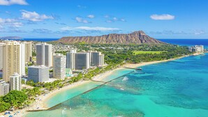 A coastal cityscape with high-rise buildings, a beach, and a prominent mountain in the background.