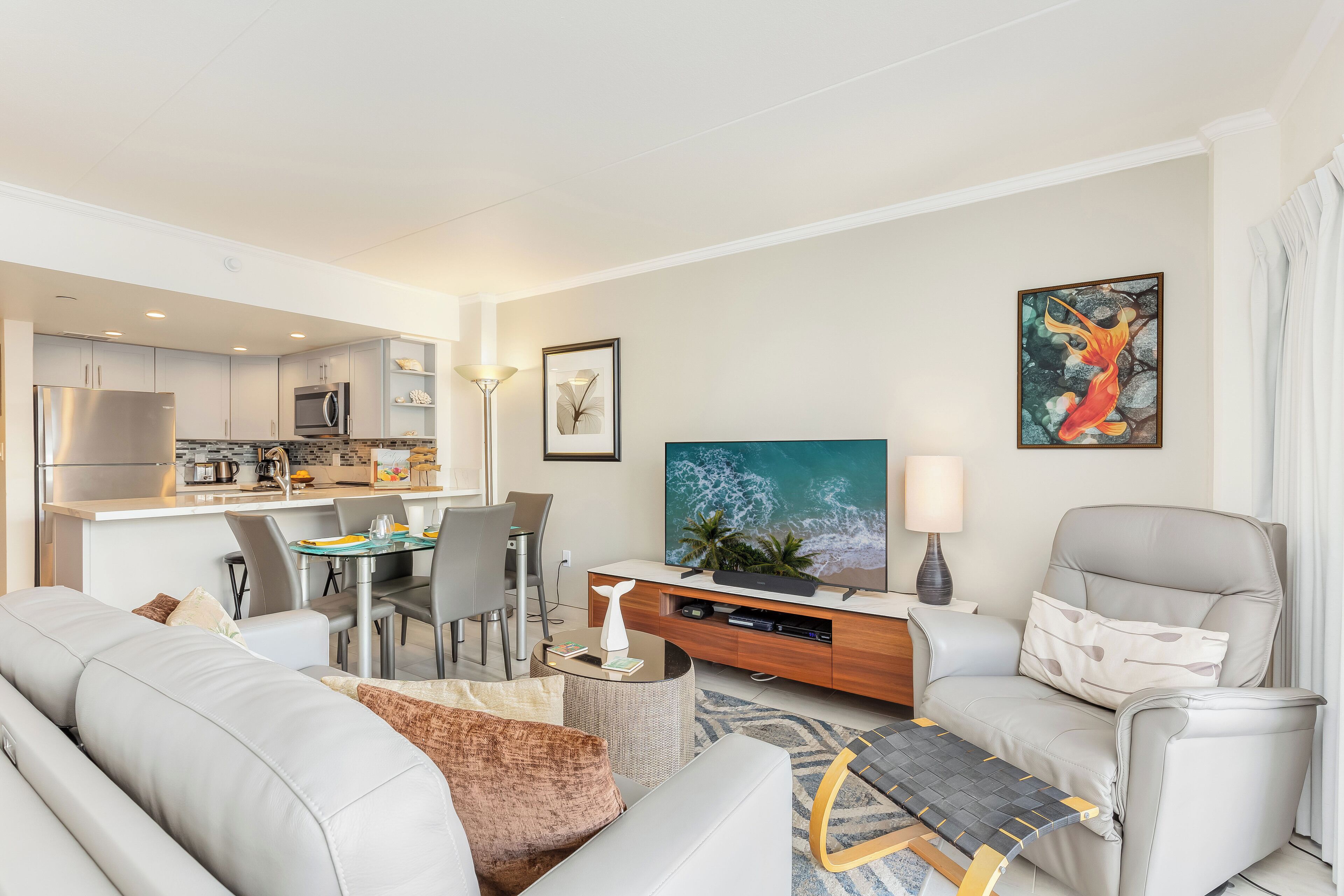 Een moderne woonkamer met een bank, fauteuil en salontafel. Er is een eethoek met een tafel en stoelen. In de achtergrond is een keuken zichtbaar.