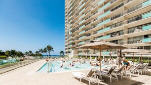 A hotel pool area with multiple levels of balconies, sun loungers, and umbrellas.