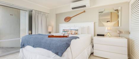 A hotel room with a bed, a bedside table, a mirror, and an air conditioning unit.