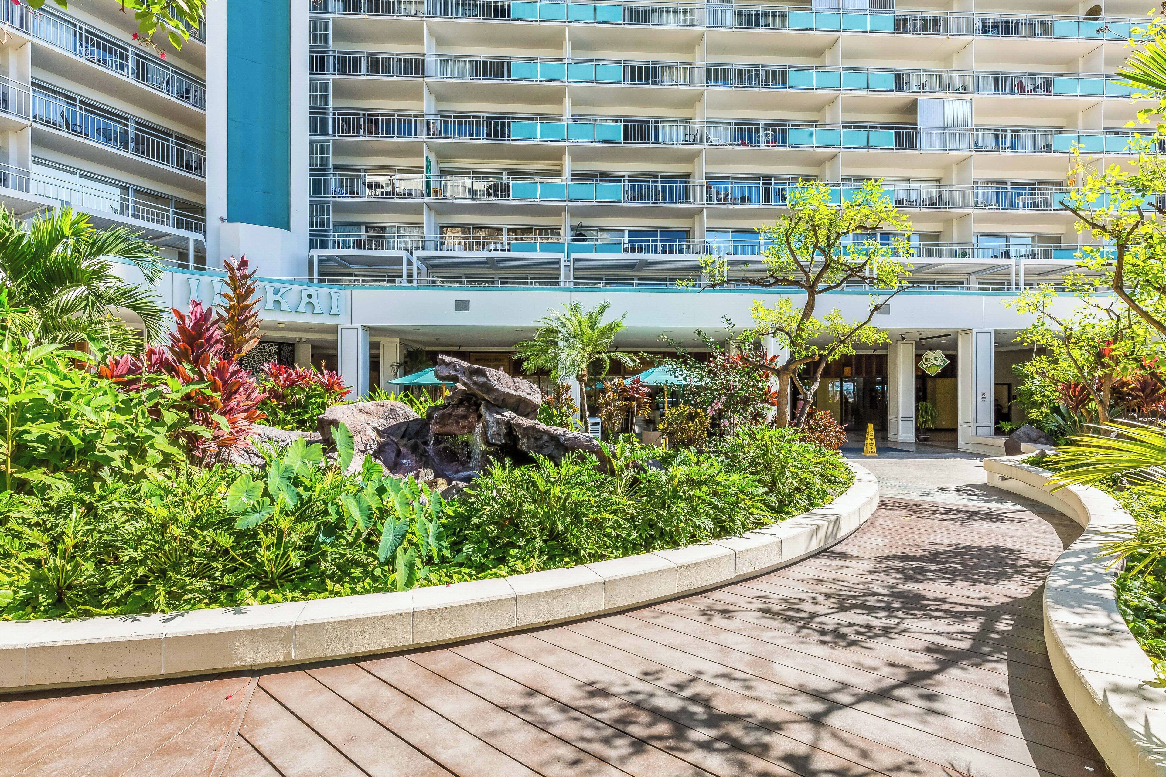 A hotel with multiple balconies, a landscaped garden with a rock feature, and a wooden pathway.