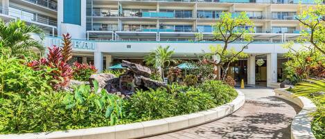 A hotel with multiple balconies, a landscaped garden with a rock feature, and a wooden pathway.