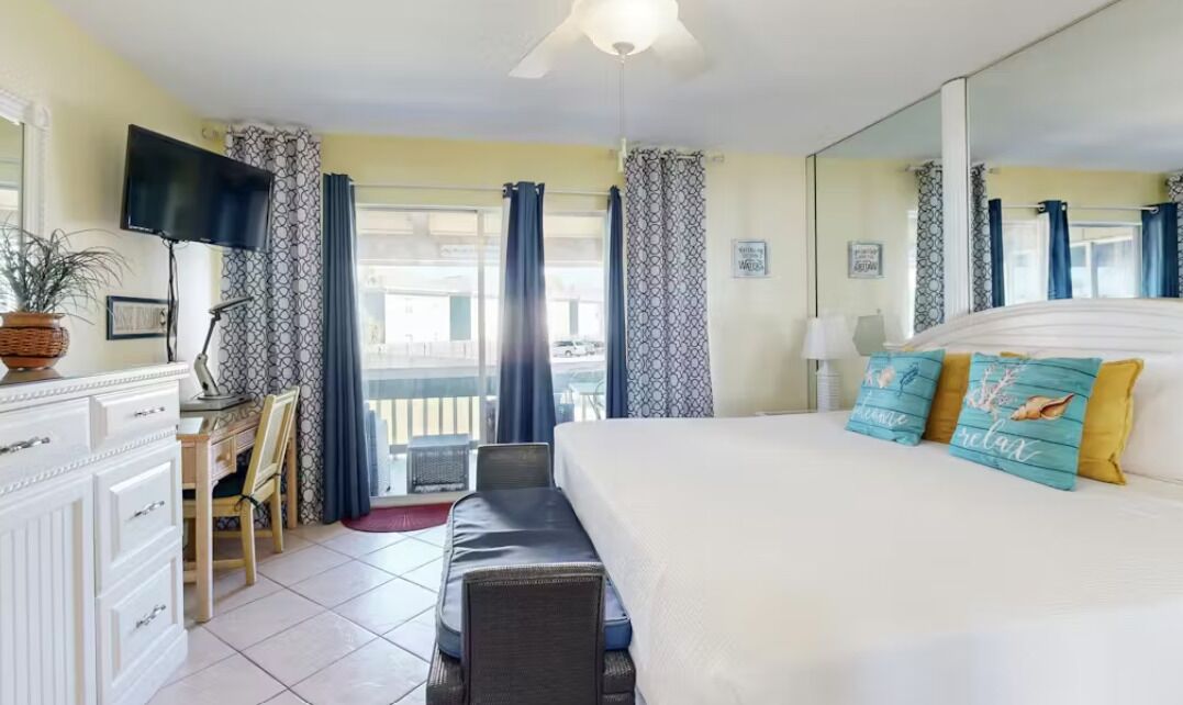 Une chambre d’hôtel équipée d’un lit, d’un bureau, d’une chaise, d’une télévision et d’un balcon avec des rideaux.