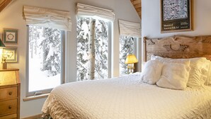 A bedroom with a large bed, wooden ceiling beams, and windows with white curtains. - Blanche's Retreat by Cottonwood Lodging (Brighton)