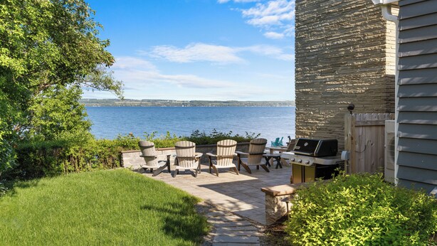 Une terrasse avec des fauteuils Adirondack, un barbecue et une vue sur l’eau.