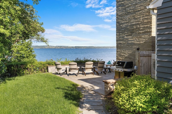 A patio with Adirondack chairs, a grill, and a view of the water.