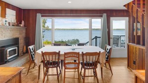 Un coin repas avec vue sur le lac, des murs en bois, une cheminée et une table dressée pour quatre personnes.