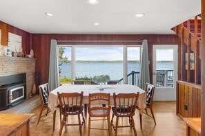 Un comedor con vista al lago, paredes de madera, chimenea y una mesa dispuesta para cuatro.