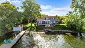 A house with a dock extending into a calm body of water, surrounded by lush greenery.