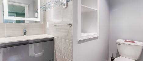 A modern bathroom with a white vanity, a glass shower enclosure, and a toilet.