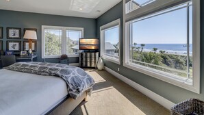 Ett sovrum med en stor säng, ett skrivbord med en lampa, en tv och utsikt över havet.