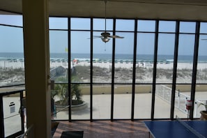 A room with large windows overlooking a beach, a ceiling fan, and a blue floor mat.
