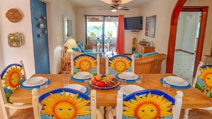 A dining area with a wooden table, chairs with sun motifs, and a view of the outdoors. - Stunning Caribbean views from the wrap around deck, at this beachfront condo! (South Akumal Beach)