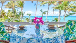 A round glass table with a blue floral pattern, surrounded by chairs with a tropical leaf design. - Stunning Caribbean views from the wrap around deck, at this beachfront condo! (South Akumal Beach)