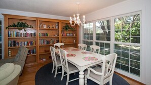 Een eetruimte met een witte tafel, vier stoelen en een kroonluchter. Boekenplanken met boeken en decoratieve objecten.