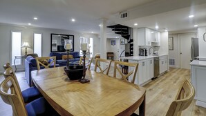 Een moderne keuken met witte kasten, een zwarte trap en een eethoek met een houten tafel en stoelen.