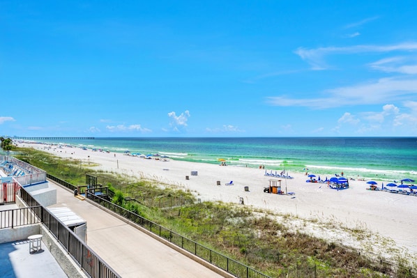 A beach with a long pier, beach umbrellas, and lounge chairs.