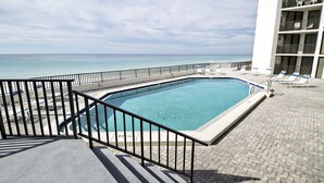 Una piscina con vista al océano, un balcón con sillones de descanso y un edificio con varios balcones.