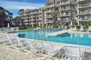 Una piscina con sillas de descanso y un edificio con varios balcones al fondo.