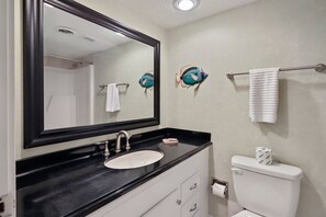 A bathroom with a black countertop, white sink, and a toilet.