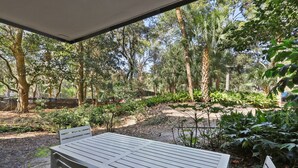Une terrasse extérieure avec une table et des chaises, entourée d’une végétation luxuriante et d’arbres.