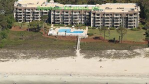 Un hôtel à plusieurs étages doté d’une piscine, situé près d’une plage au rivage sablonneux.