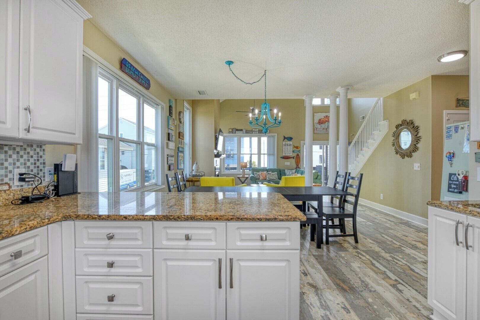 A spacious kitchen with granite countertops, white cabinetry, and a dining area with a yellow table and chairs.